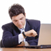Man checking watch in front of laptop